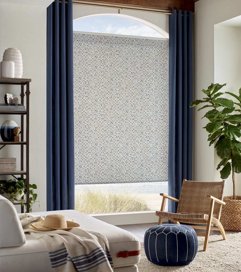 fabric roller shade in multi-colored pattern with blue side draperies on a gold rod