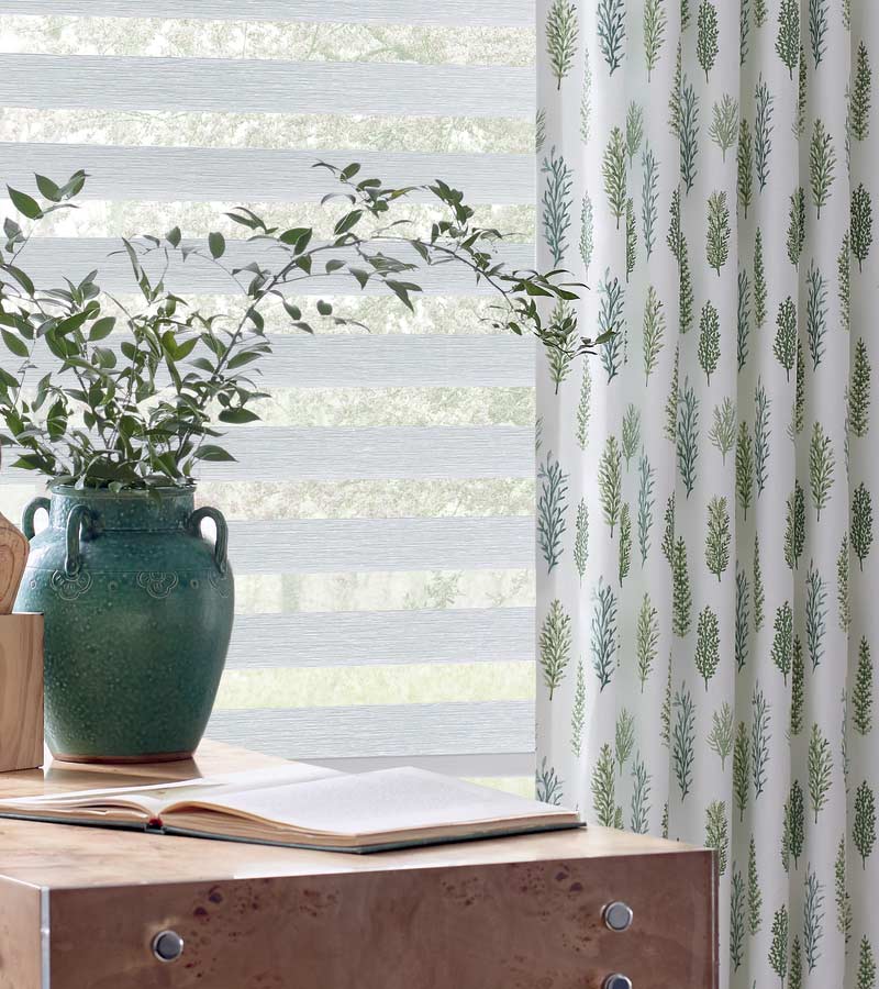 close up window scene with white zebra shades and white draperies with green embroidery