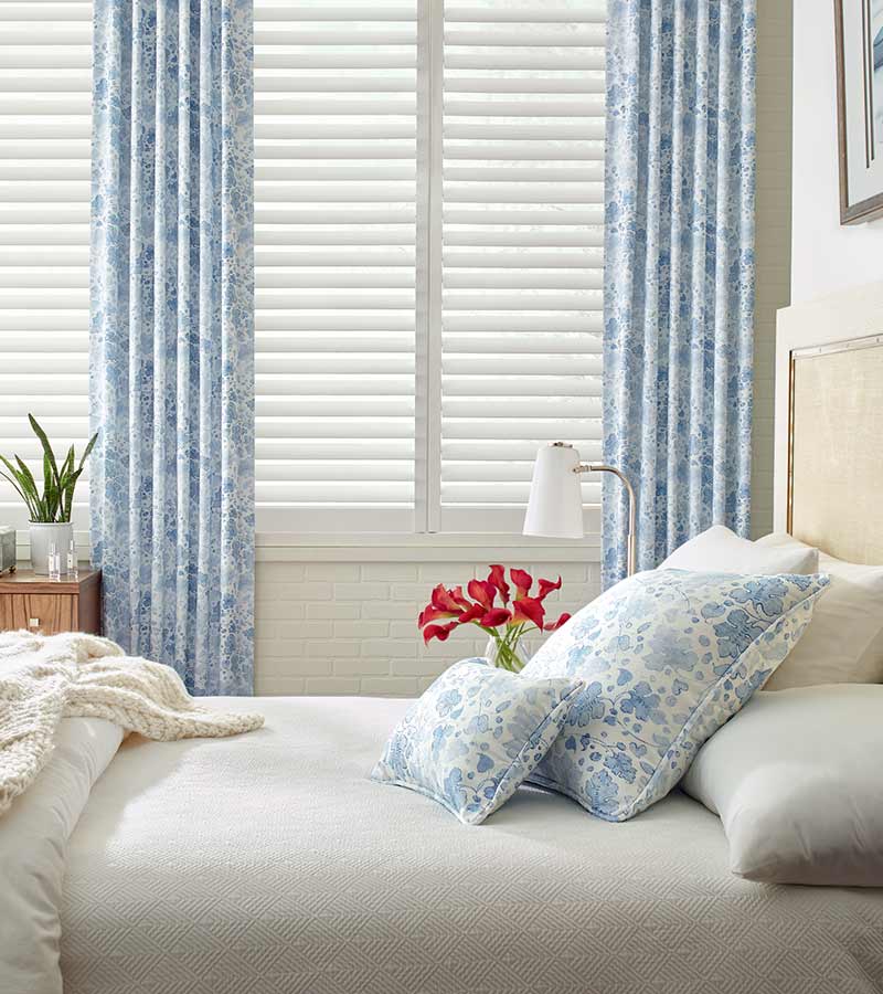 coastal guest bedroom white plantation shutters framed by blue floral curtains in chicago, il
