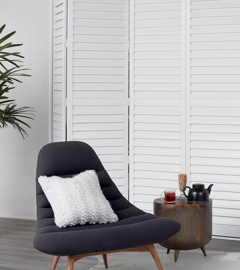 bi-fold custom white plantation shutters behind lounge chair Chicago, IL