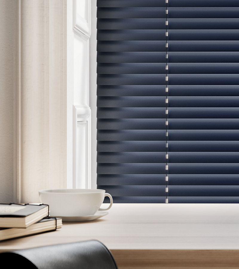 detail of slate color horizontal blind next to coffee cup and notebooks