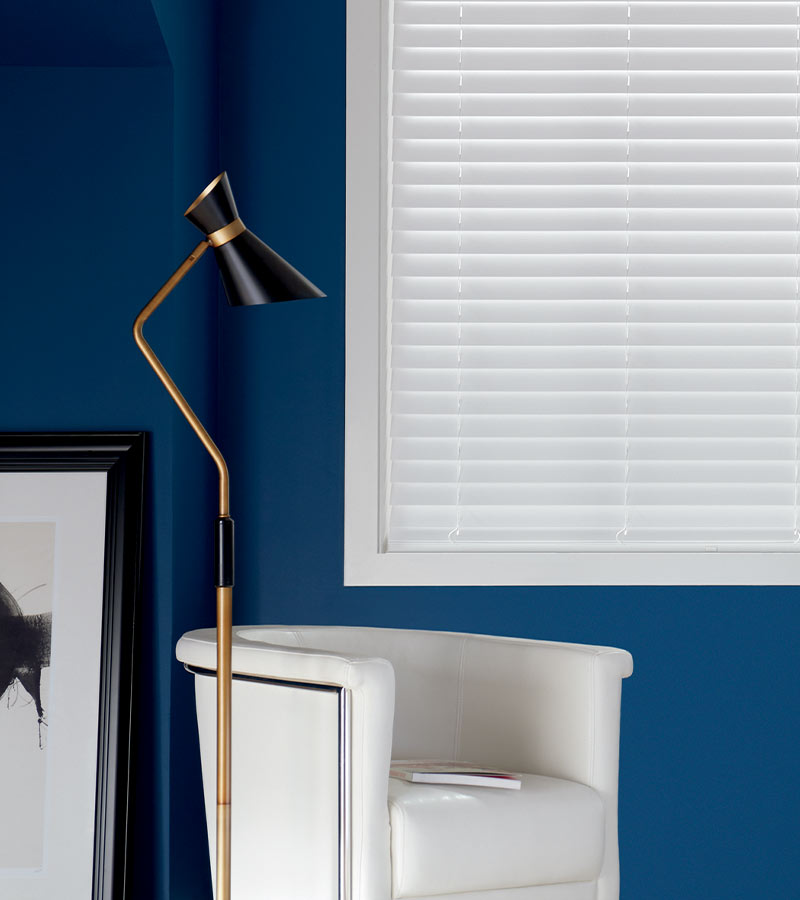 white composite blinds next to white fabric chair and modern lamp