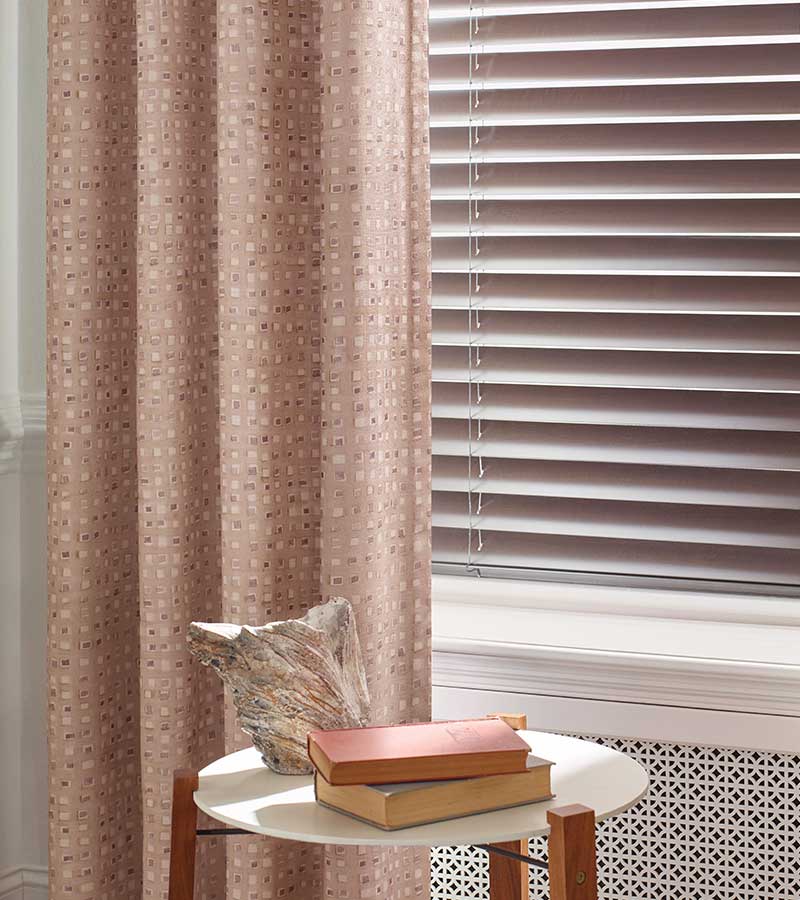 composite blinds next to layered pink drapery panels