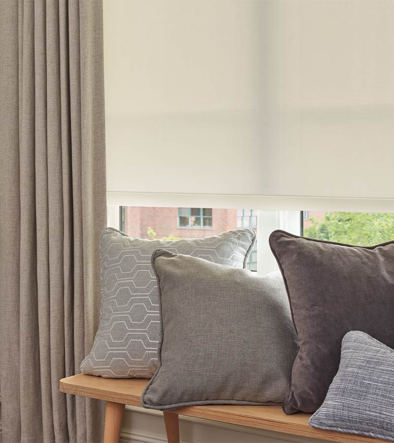 close up of pillows on bench with drapery panels in front of rolled down screen shade