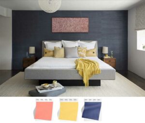 large bedroom with deep blue grasscloth wallpaper and coral colored art