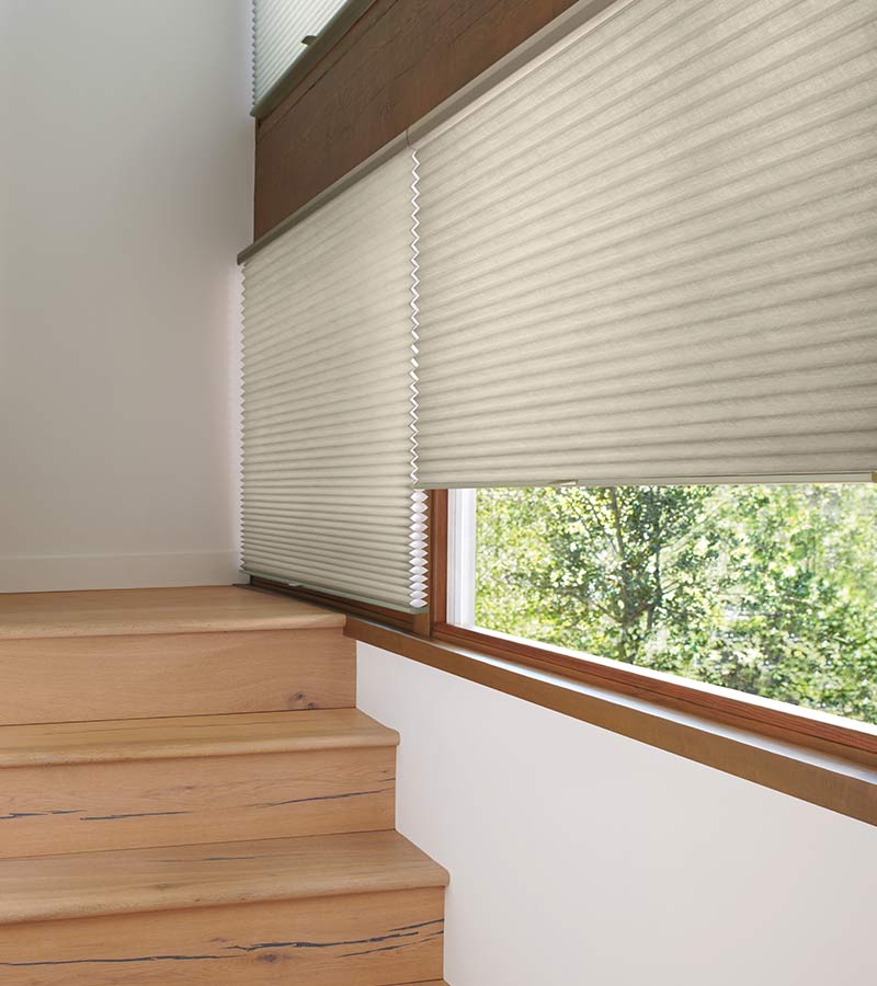 windows over stairwell covered by a beige window shade with honeycomb cells