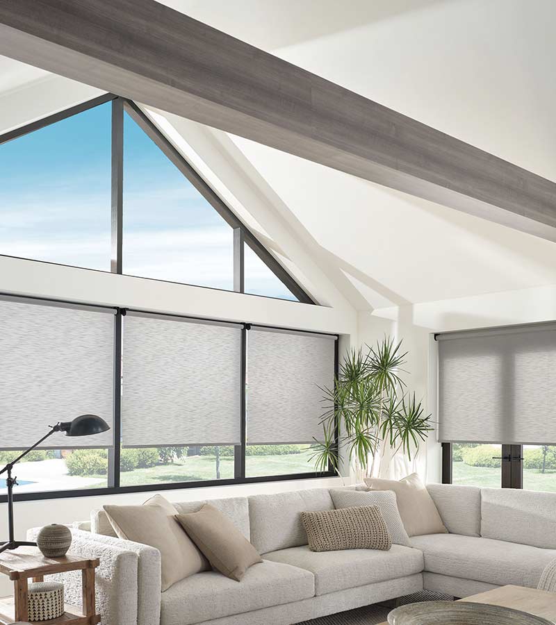 angled windows with gray shades in lofted ceiling family room with neutral couch and accents