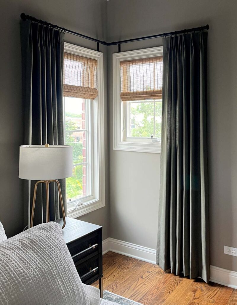 dark green drapery with woven wood roman shades for corner windows
