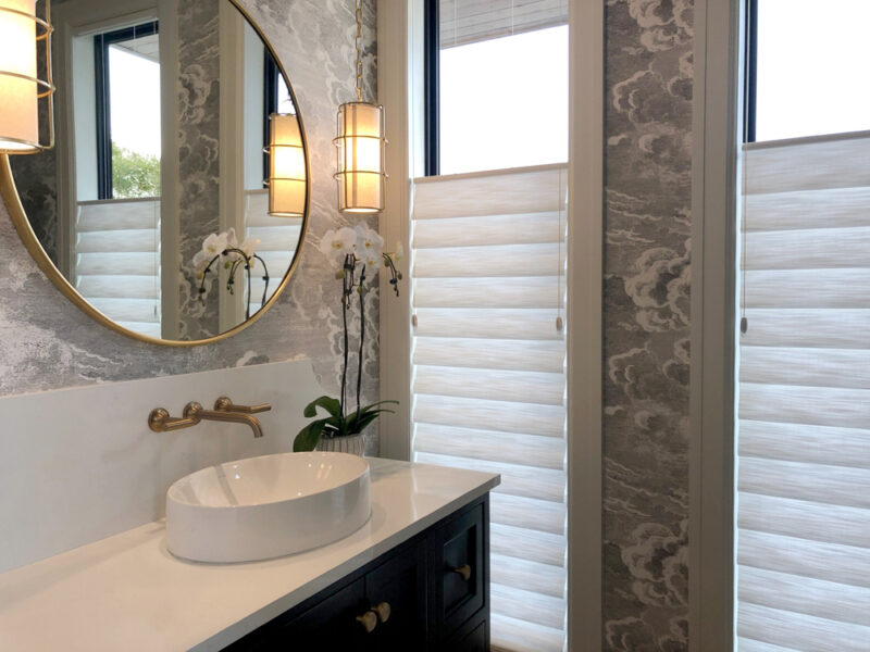 bathroom with gray wallpaper circle mirror and top down roman shades on narrow windows in westlake village