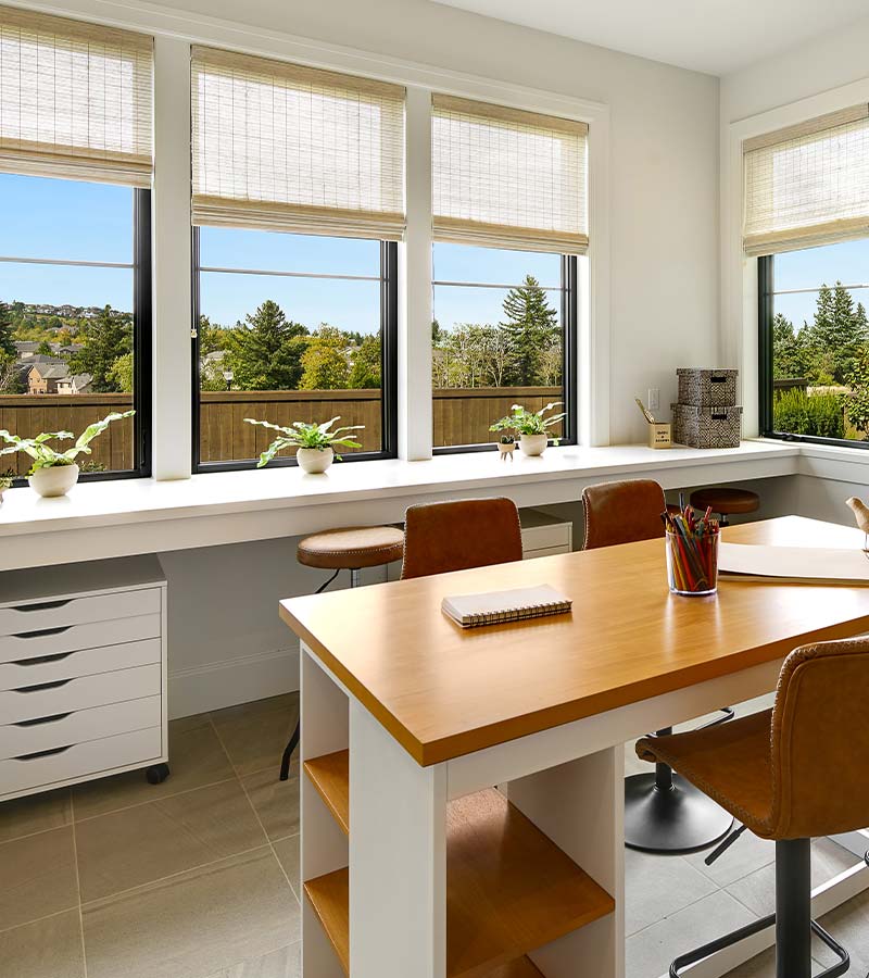 affinity-homes-design-portland-provenance-woven-wood-shades-skyline-window-coverings Portland home office with woven wood shades on multiple windows in a bright three season room