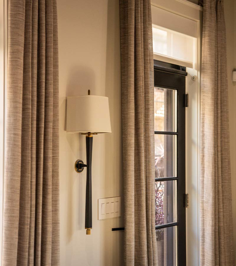 urbane-home-dee-thompson-carole-fabrics-drapery-skyline-window-coverings-trade-program close up of draperies and roller shades over patio doors for light and privacy control
