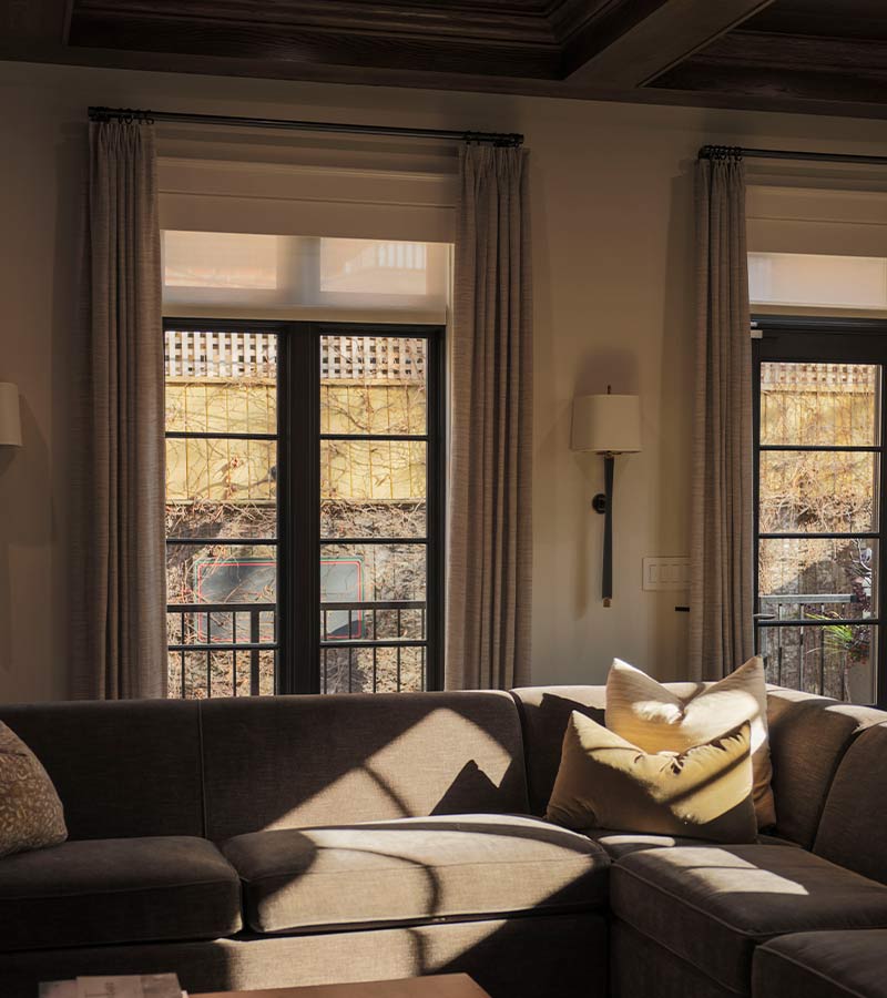 urbane-home-dee-thompson-layered-roller-shades-drapery-skyline-window-coverings-trade-program Roller shades layered with drapery over dark framed french doors