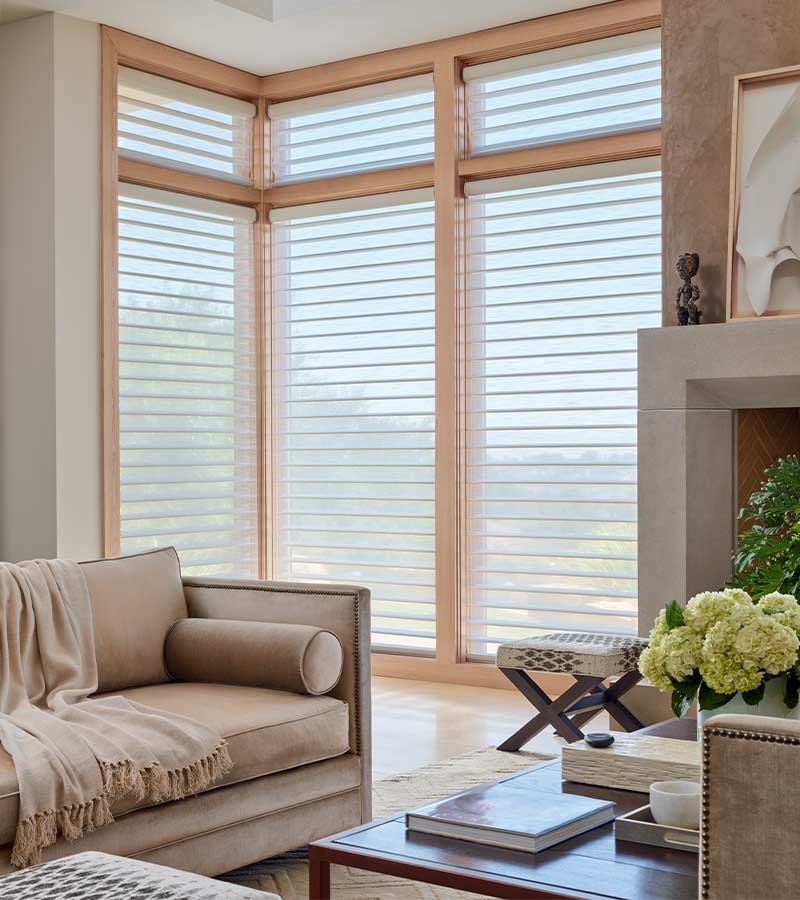 Light-filtering Silhouette window shades on tall corner windows, creating a warm glow in a modern living room with sofa and fireplace