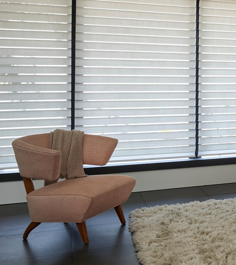 Hunter Douglas Silhouette sheer window shades behind a modern accent chair, gently filtering daylight through layered fabric vanes